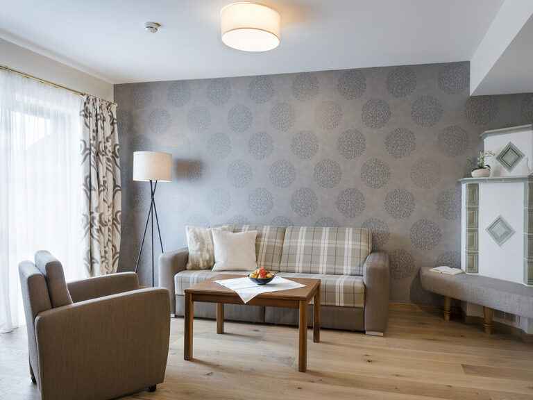 Komfortabler Wohnbereich in der Silberbergsuite des Wellnesshotels Mooshof im Bayerischen Wald mit einer gemütlichen Sitzgelegenheiten vor einem Kachelofen.